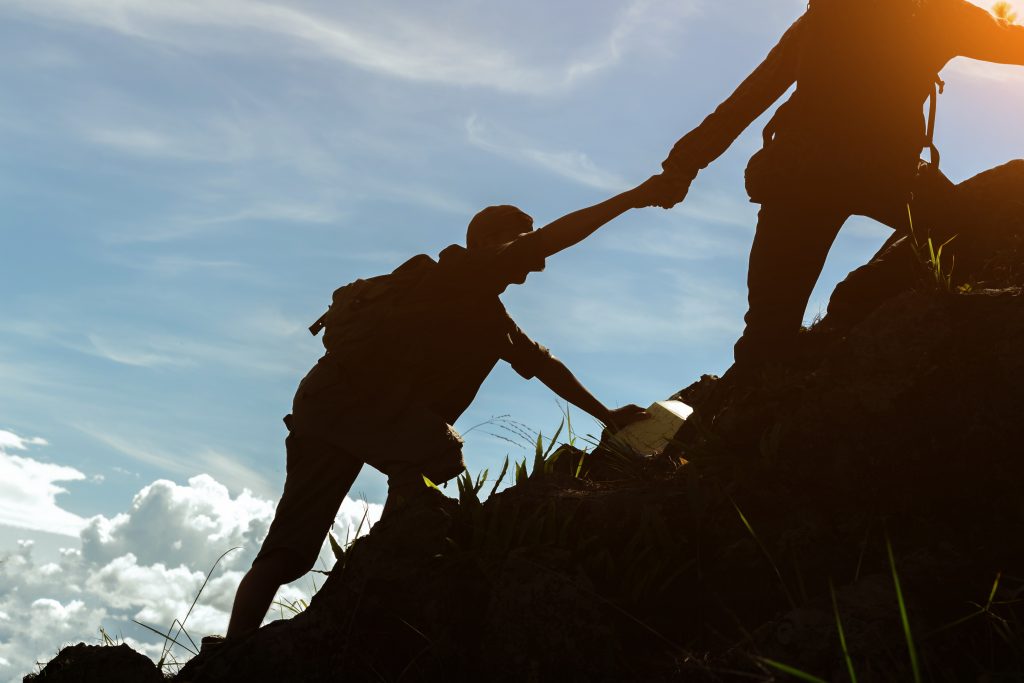 Help and assistance concept.Two male hikers climbing up mountain cliff and one of them giving helping hand.